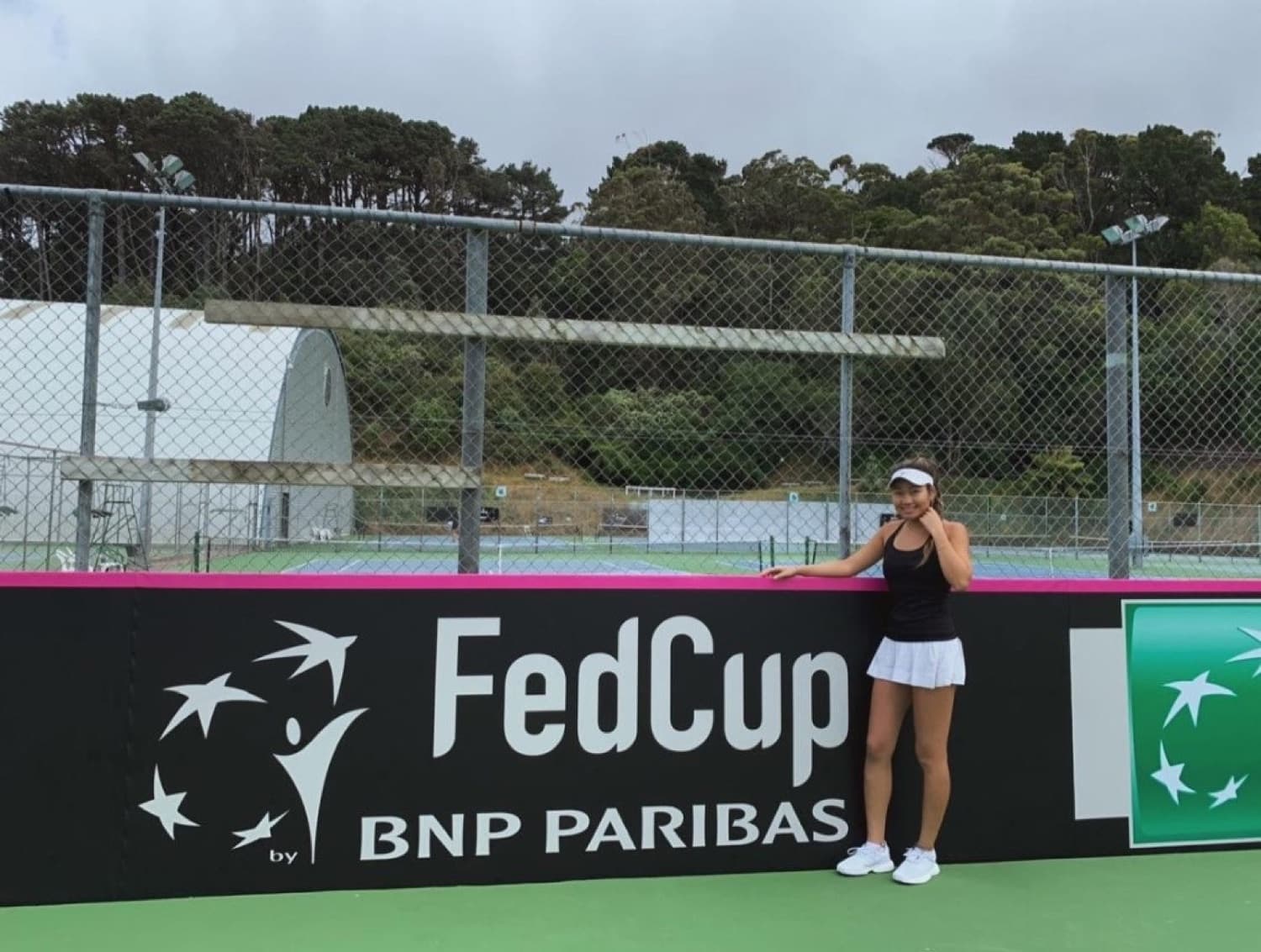 Bolor at a Fed Cup by BNP Paribas tie, leaning on the courtside banner.